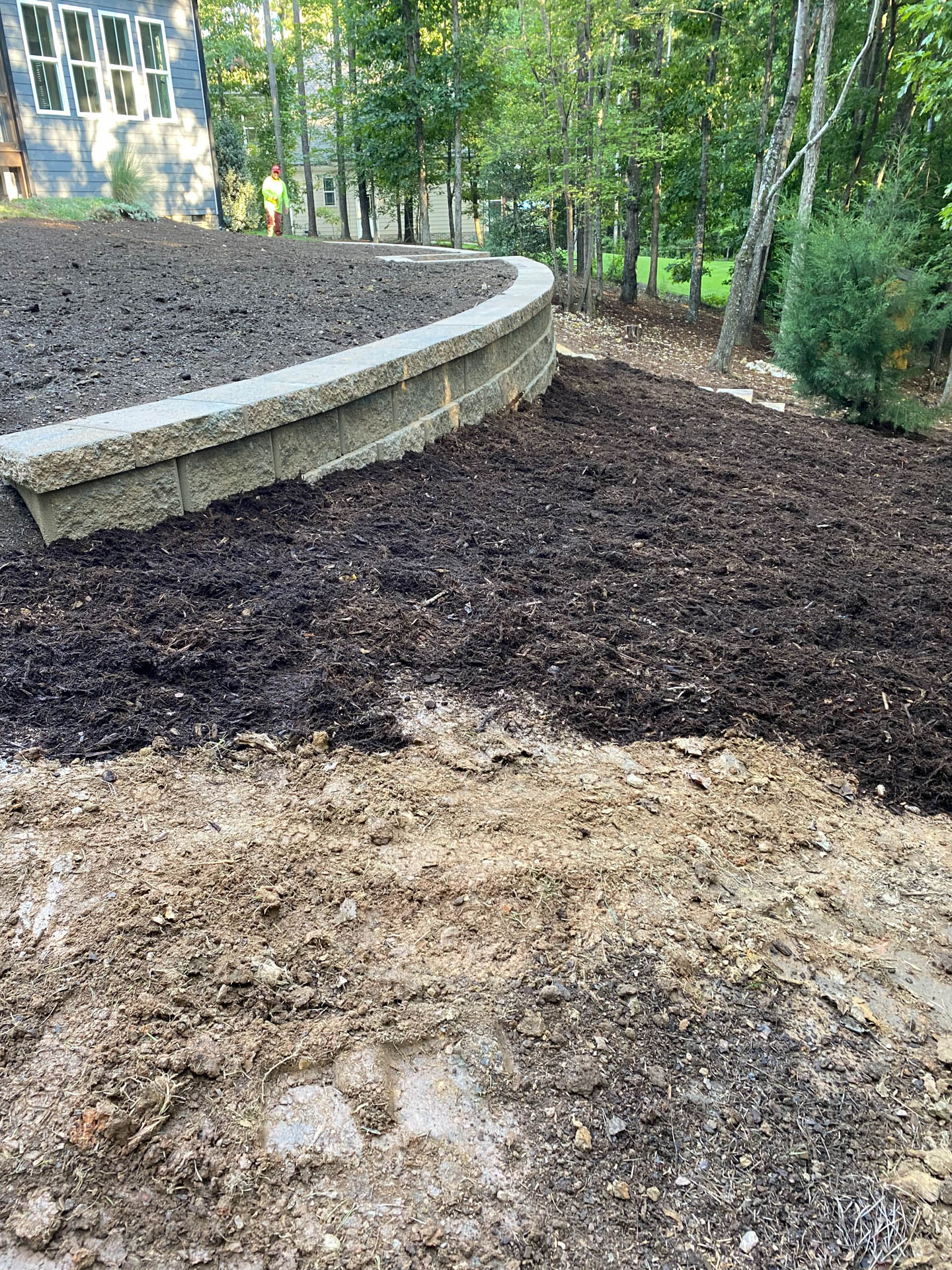 Landscaping: retaining wall with fresh mulch; exposed dirt in the foreground.