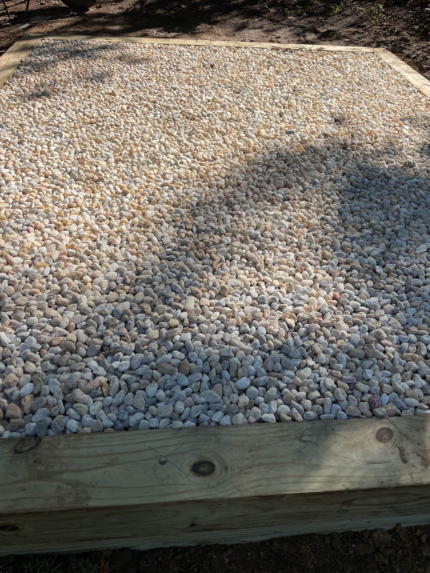 Raised wooden frame filled with small, light-colored pebbles.
