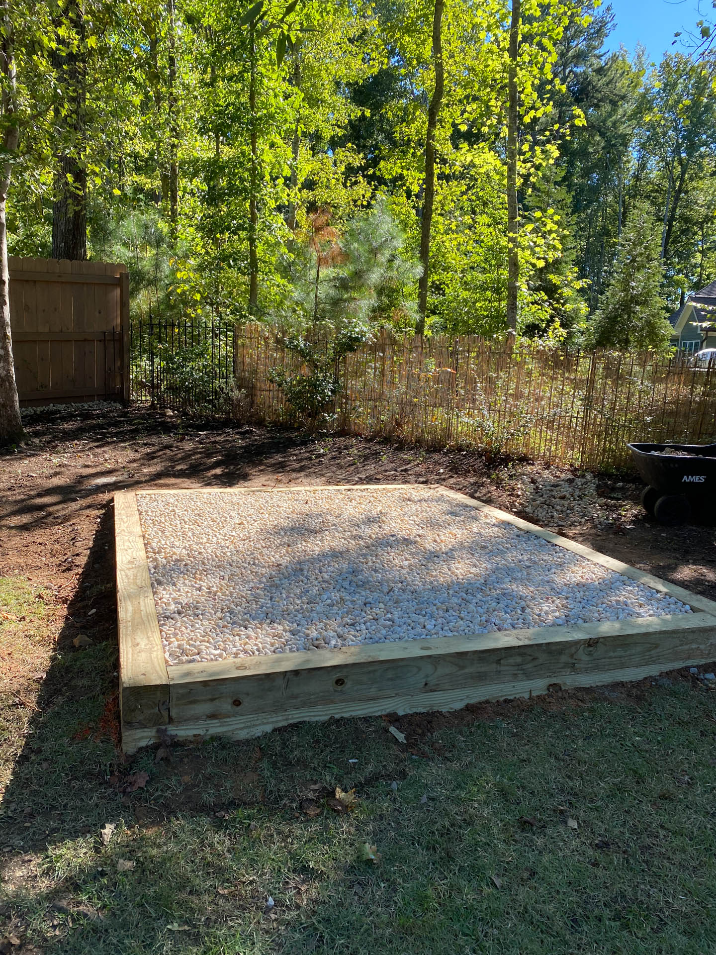 Gravel-filled wooden platform in a yard, surrounded by grass and trees; fence in background.