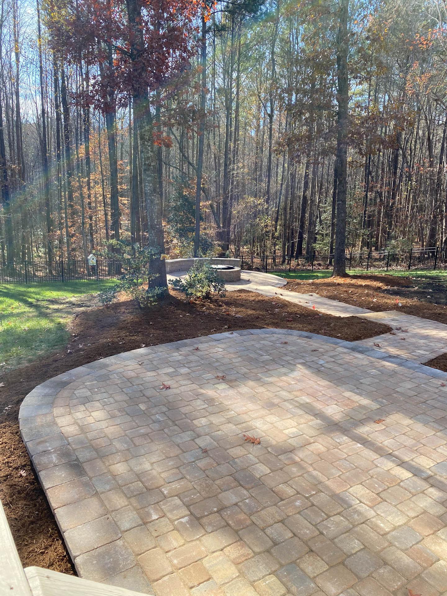 Brick patio with curved edges, leading to a path and a wooded background.