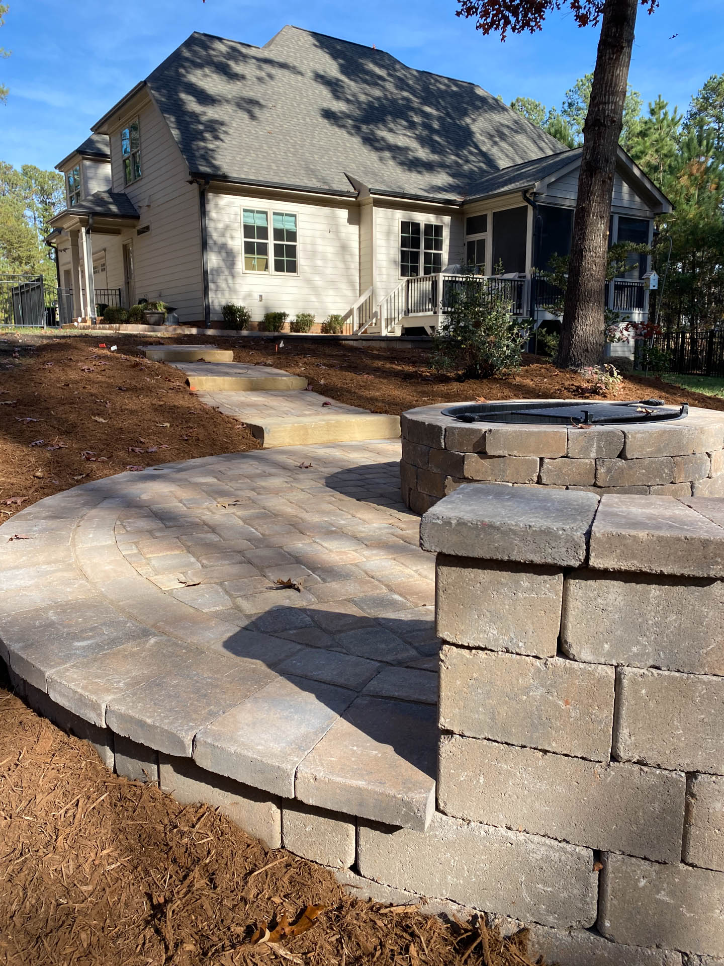 Brick patio and fire pit beside a two-story beige house with a dark gray roof.