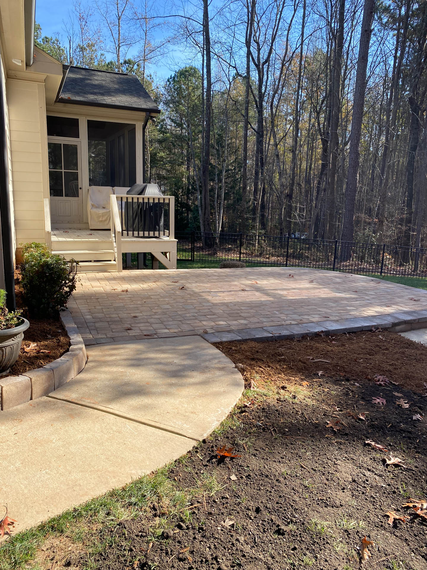A paved patio next to a house with a screened porch, surrounded by trees.