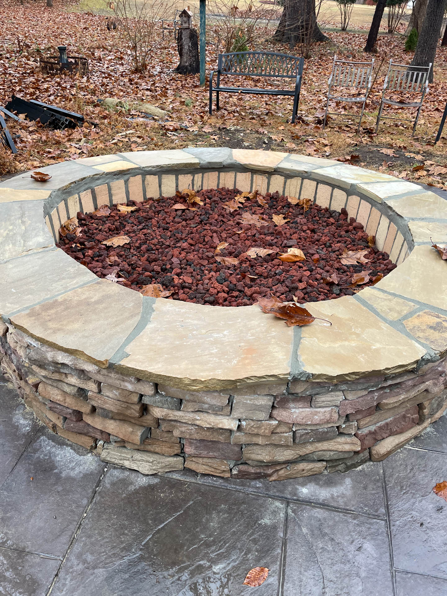 Stone fire pit with brown lava rocks, surrounded by paving stones, outside in a yard.
