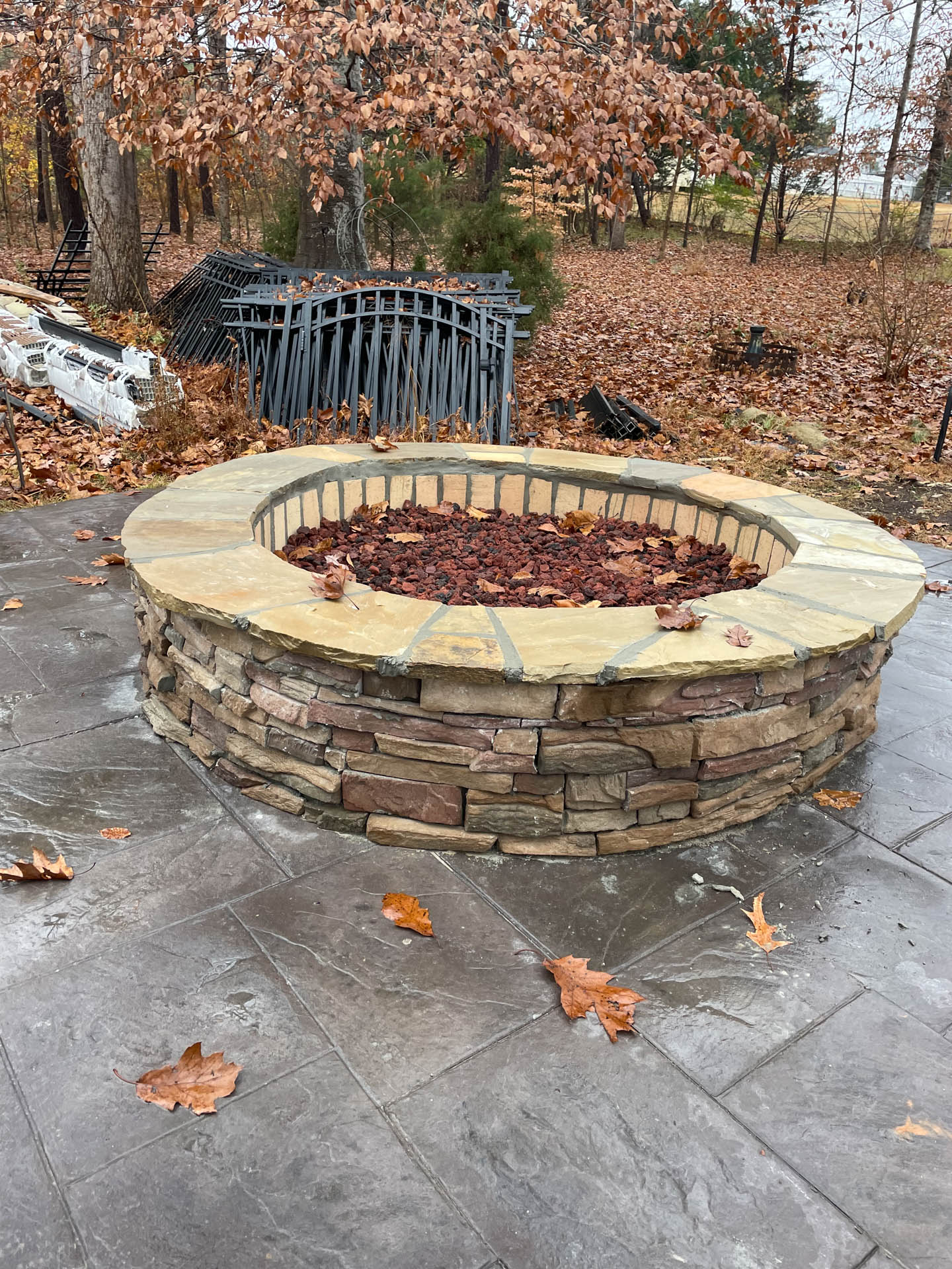 Circular stone fire pit on a gray patio with scattered fallen leaves.