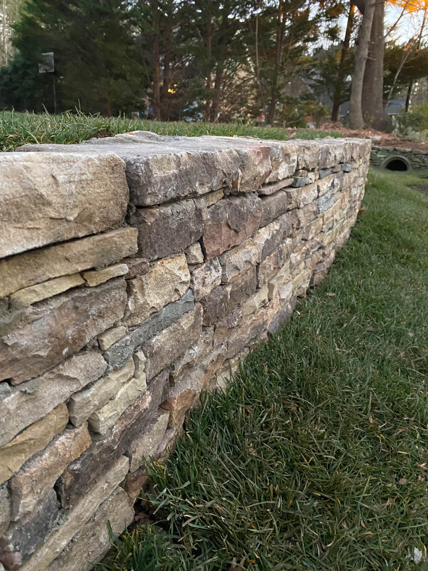 Stone retaining wall in a grassy yard, with trees in the background.