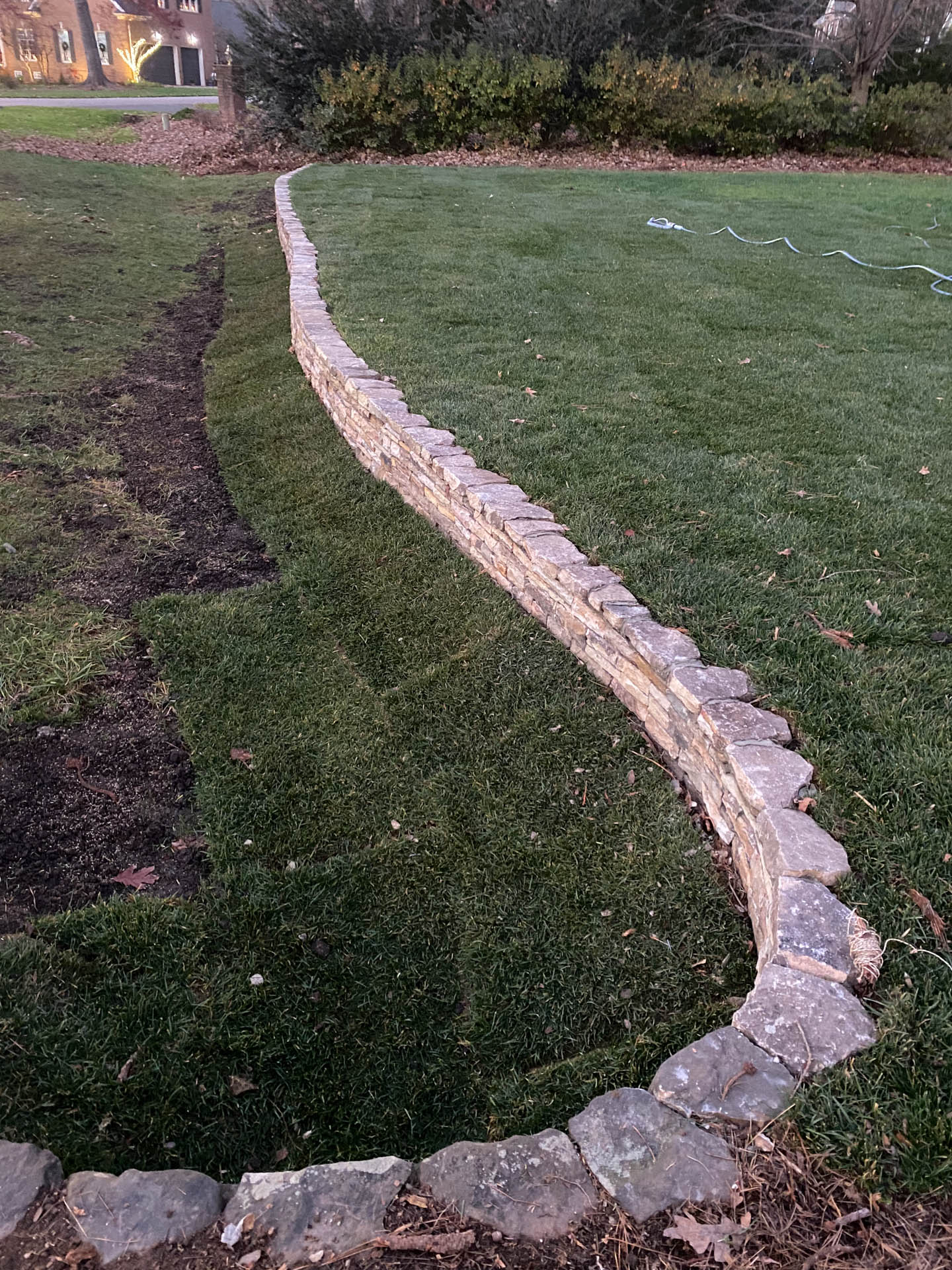 Stone wall edging a lawn. Newly turned soil on one side.
