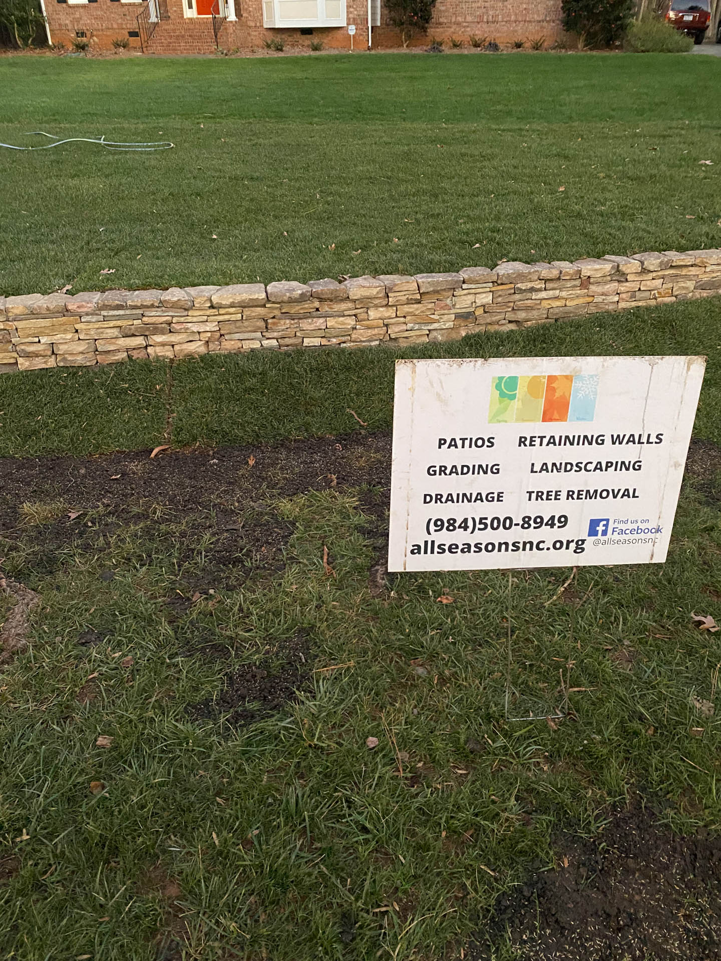 Sign advertising landscaping services in front of a stone retaining wall and lawn.