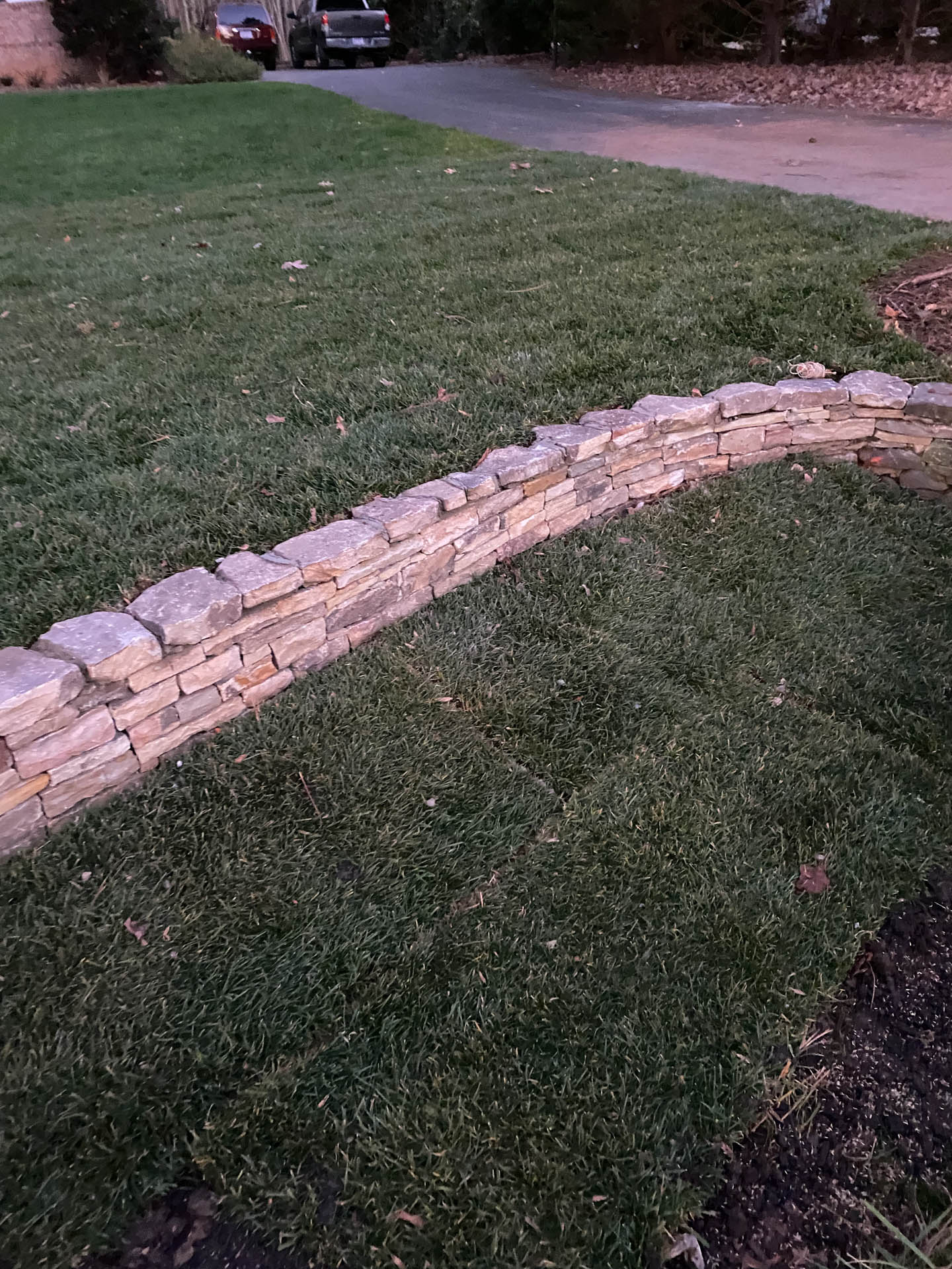 Stone retaining wall bordering grass lawn and driveway.