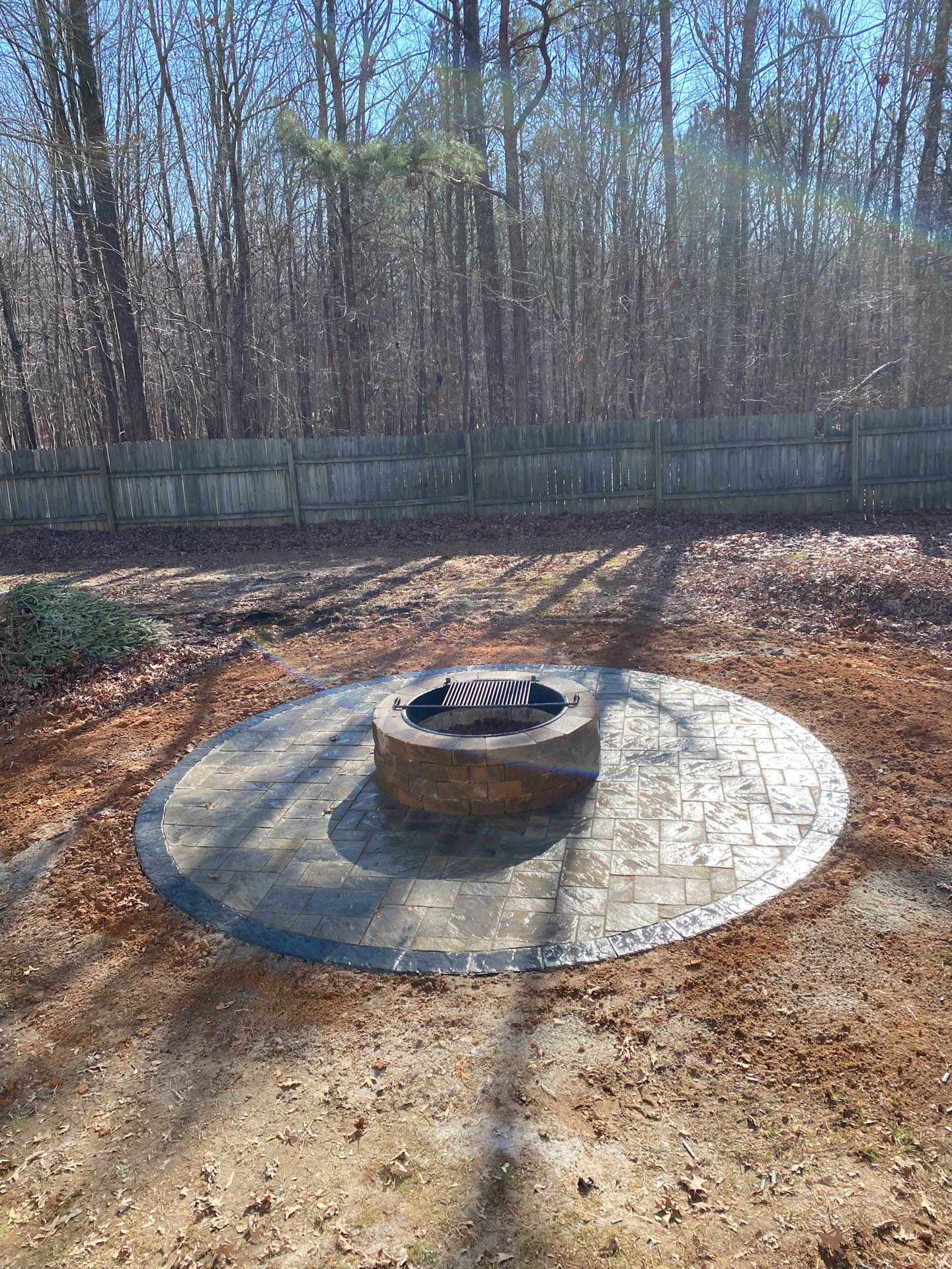 Circular stone patio with fire pit and grill in backyard.