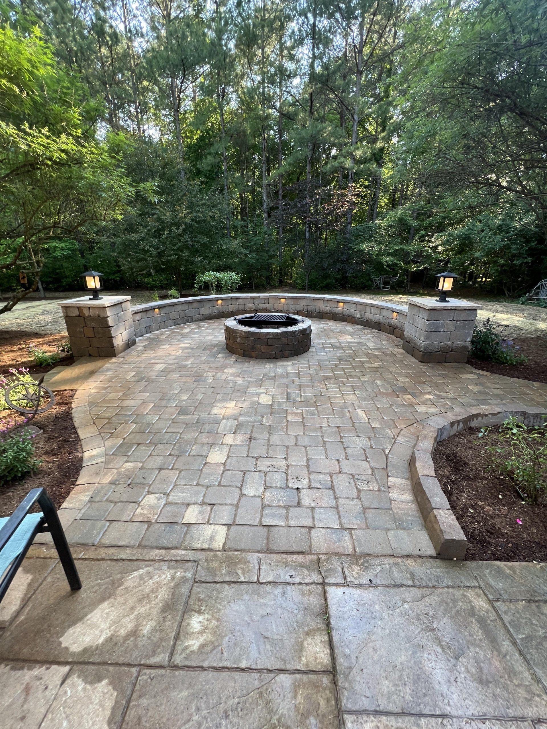 Stone patio with curved wall and fire pit, surrounded by trees.
