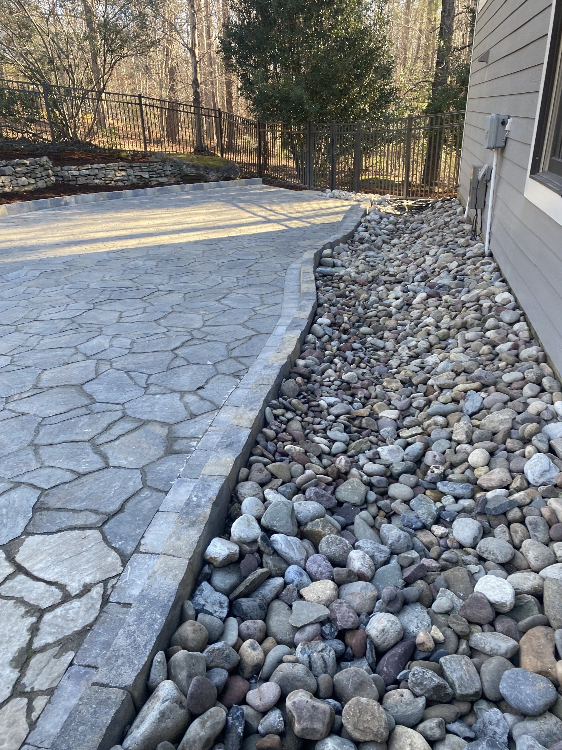 Stone patio next to a rock garden and a light gray house. Trees are in the background.