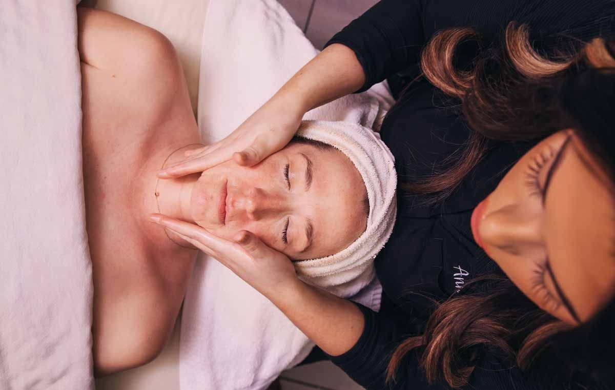 Spa therapist giving a facial massage to a client with a towel wrapped around her head