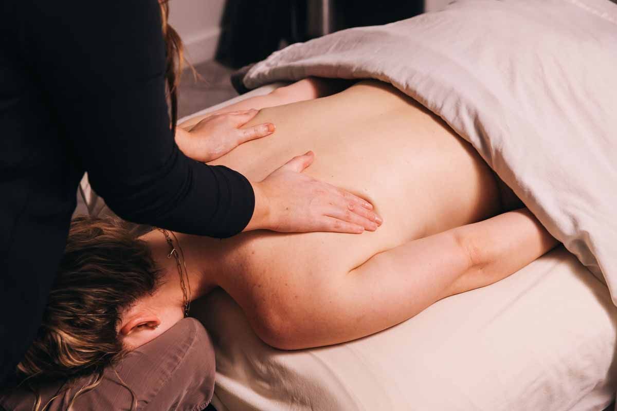 Massage therapist pressing a client’s back with a warm towel draped over the body