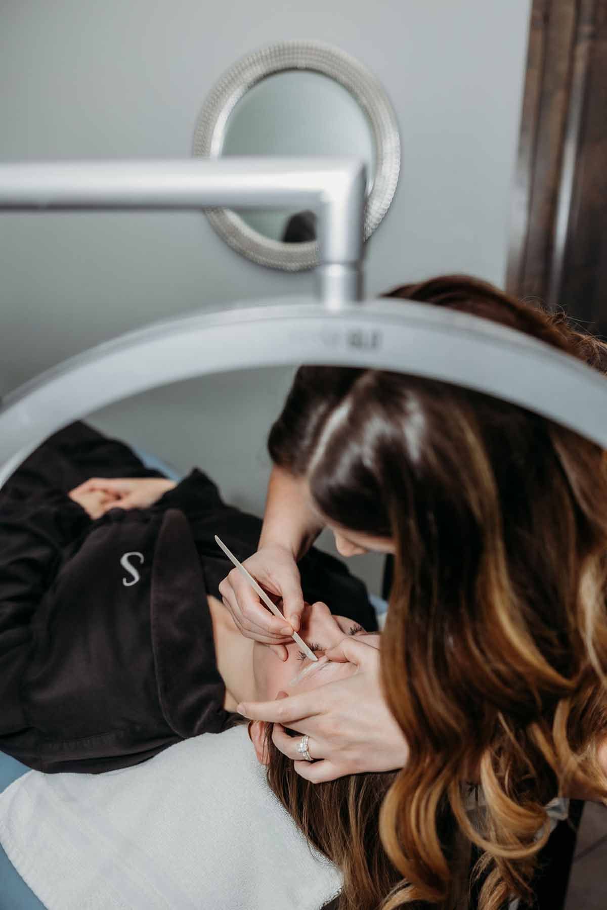 Person getting a facial treatment while lying under a magnifying lamp in a spa room