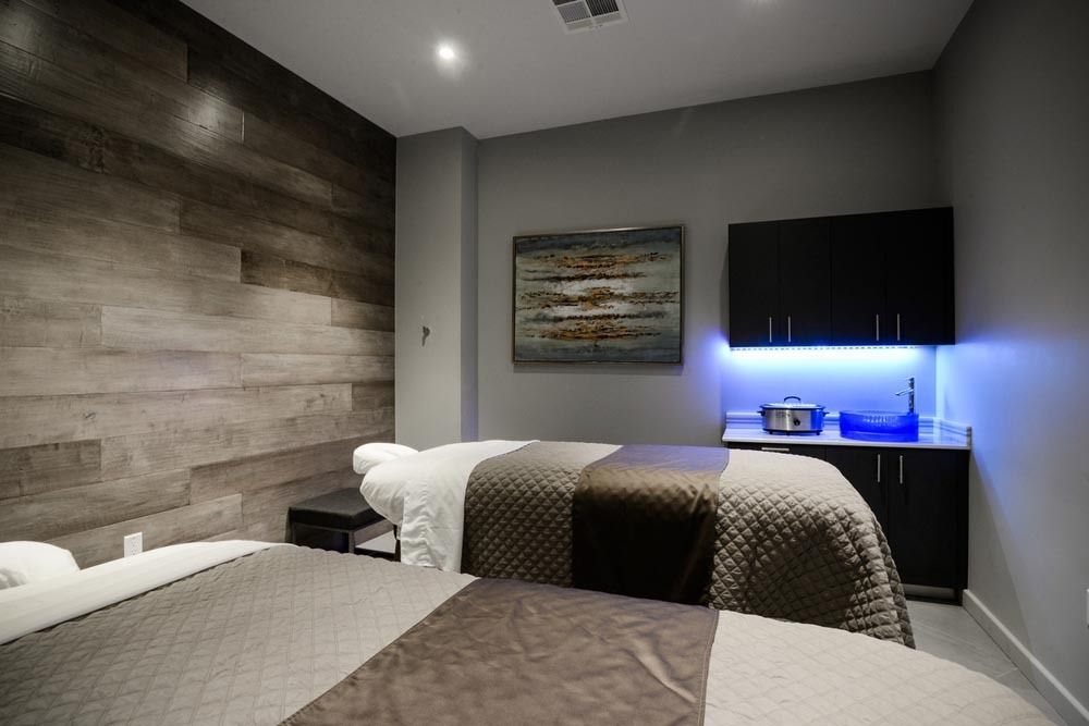 Modern bedroom with gray walls, textured wood accent wall, neatly made bed, and blue-lit TV area