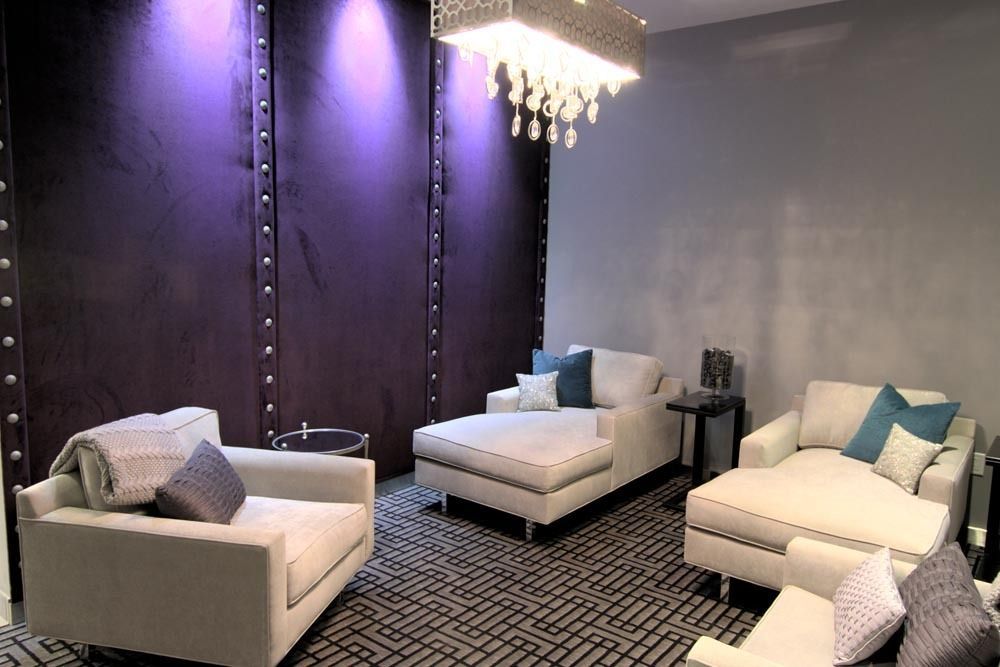 Modern lounge with white sofas, purple walls, patterned rug, and a chandelier under soft lighting