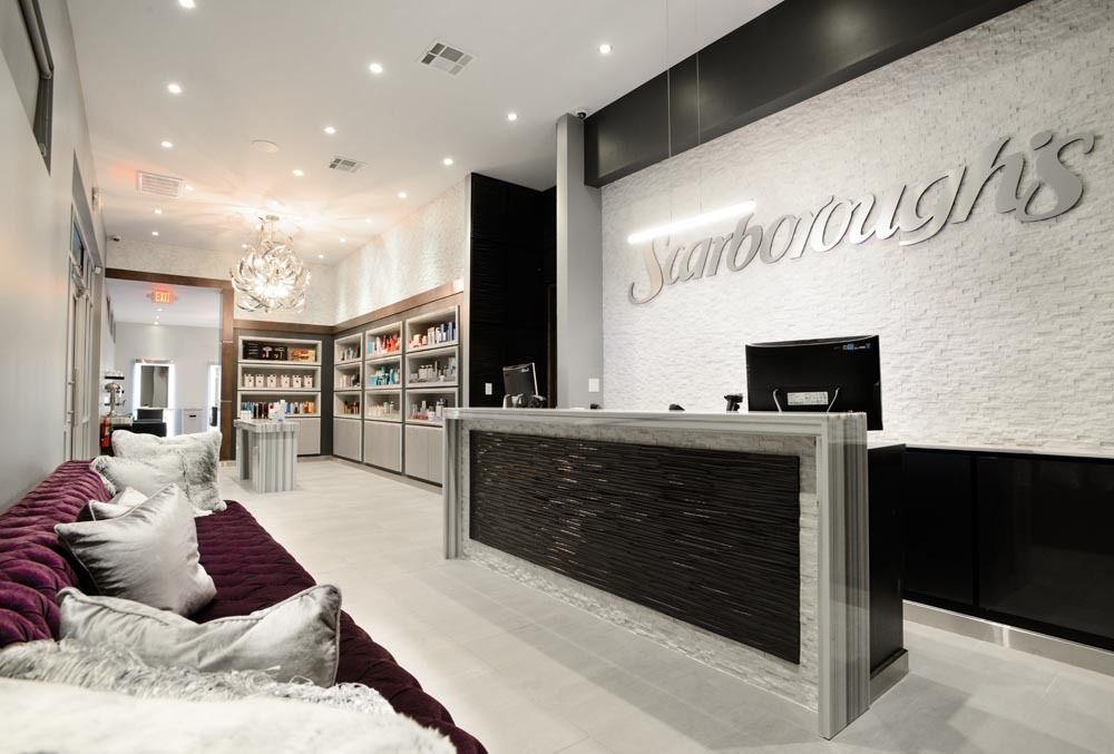 Modern spa reception with white walls, black counter, pink seating, and lit shelves