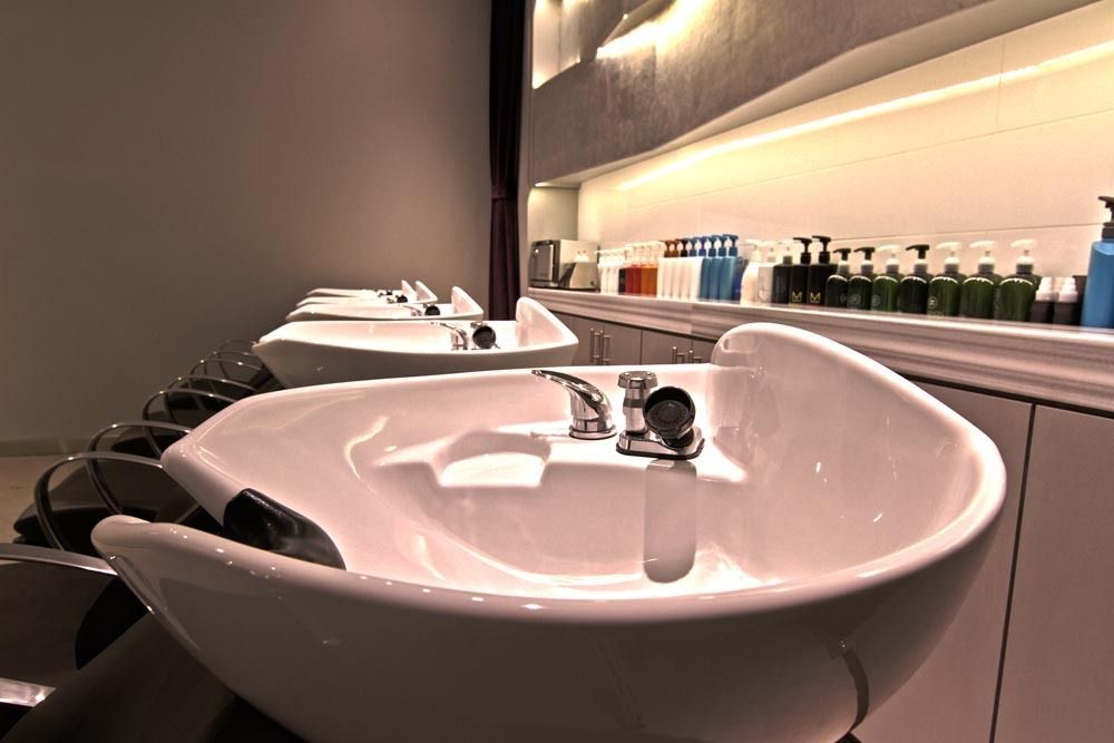 Modern bathroom with row of white sinks and mirrors, lit shelves of toiletries along the wall