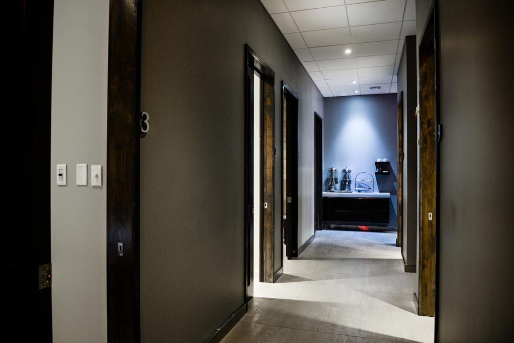Empty office hallway with dark walls, open doors, and a lit room at the end.