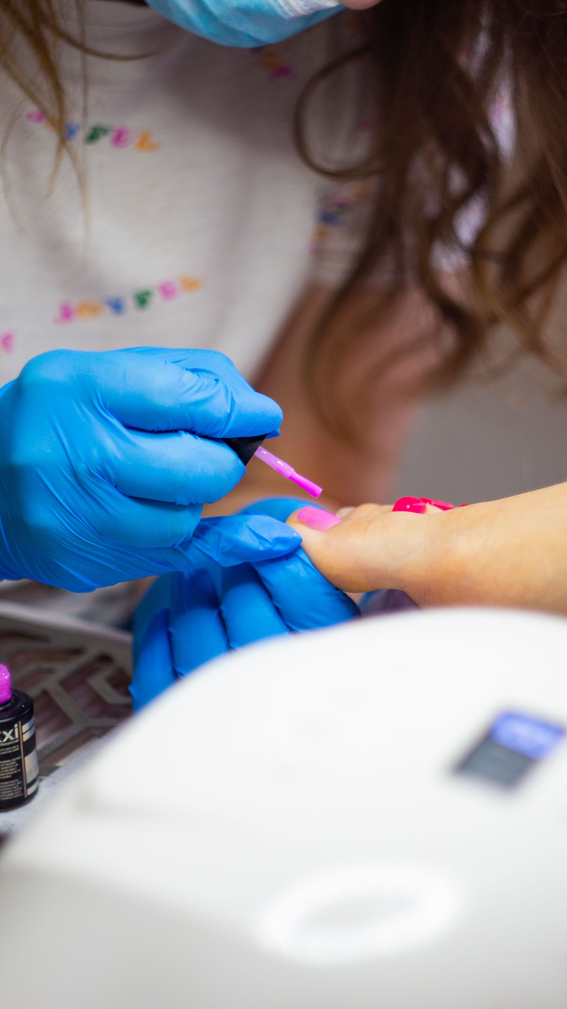 Gloved hands painting pink toenails on a foot with a small brush