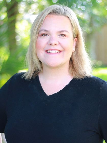 Smiling blonde woman in a black top standing outdoors with a blurred green background
