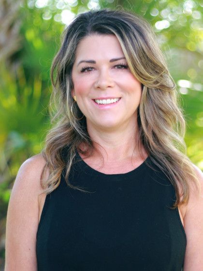 Smiling woman in a black sleeveless top standing outdoors against a blurred green background