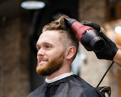 Man getting a haircut with electric clippers in a barbershop, smiling in profile