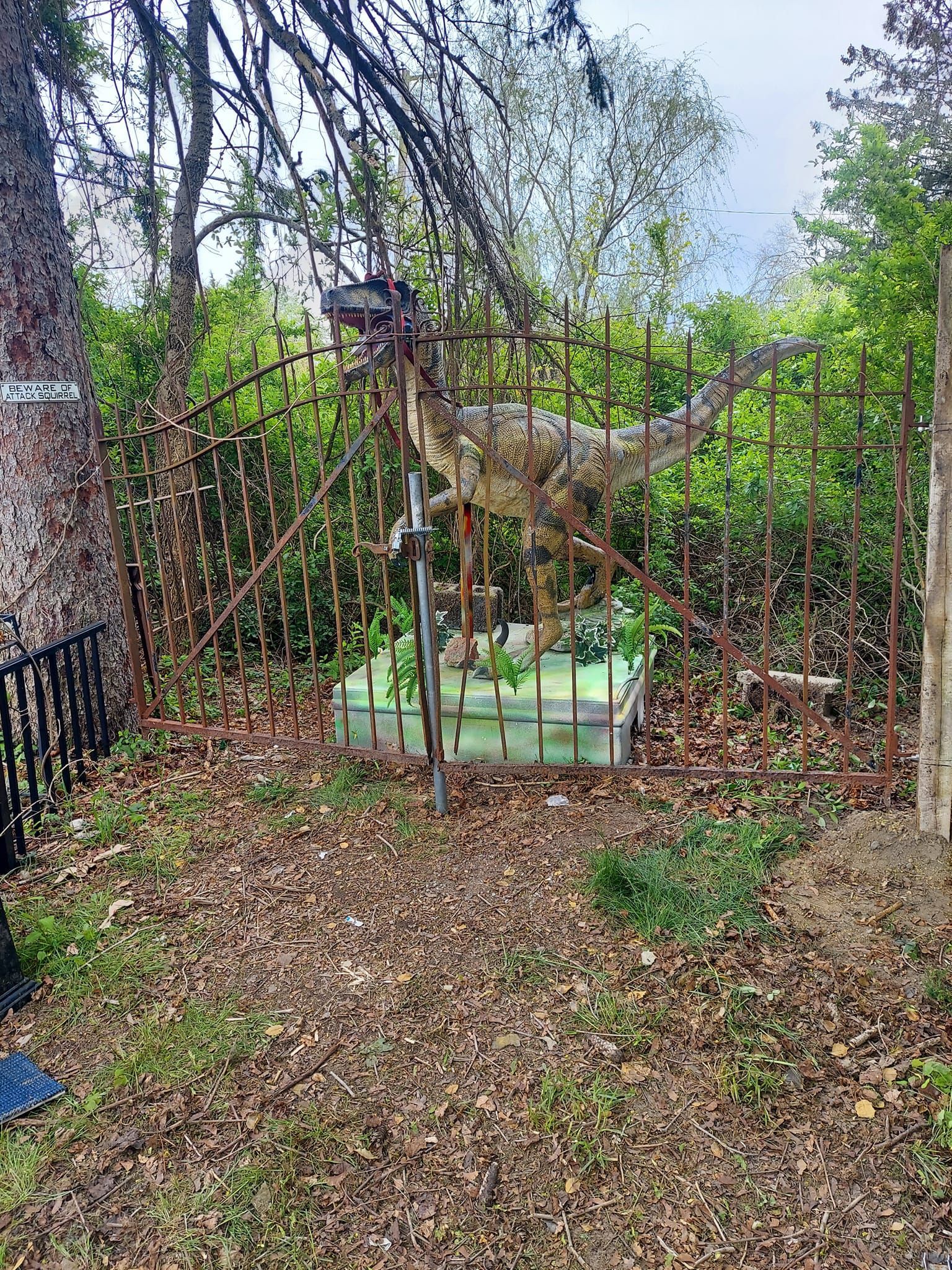 A statue of a dinosaur is behind a rusty gate.