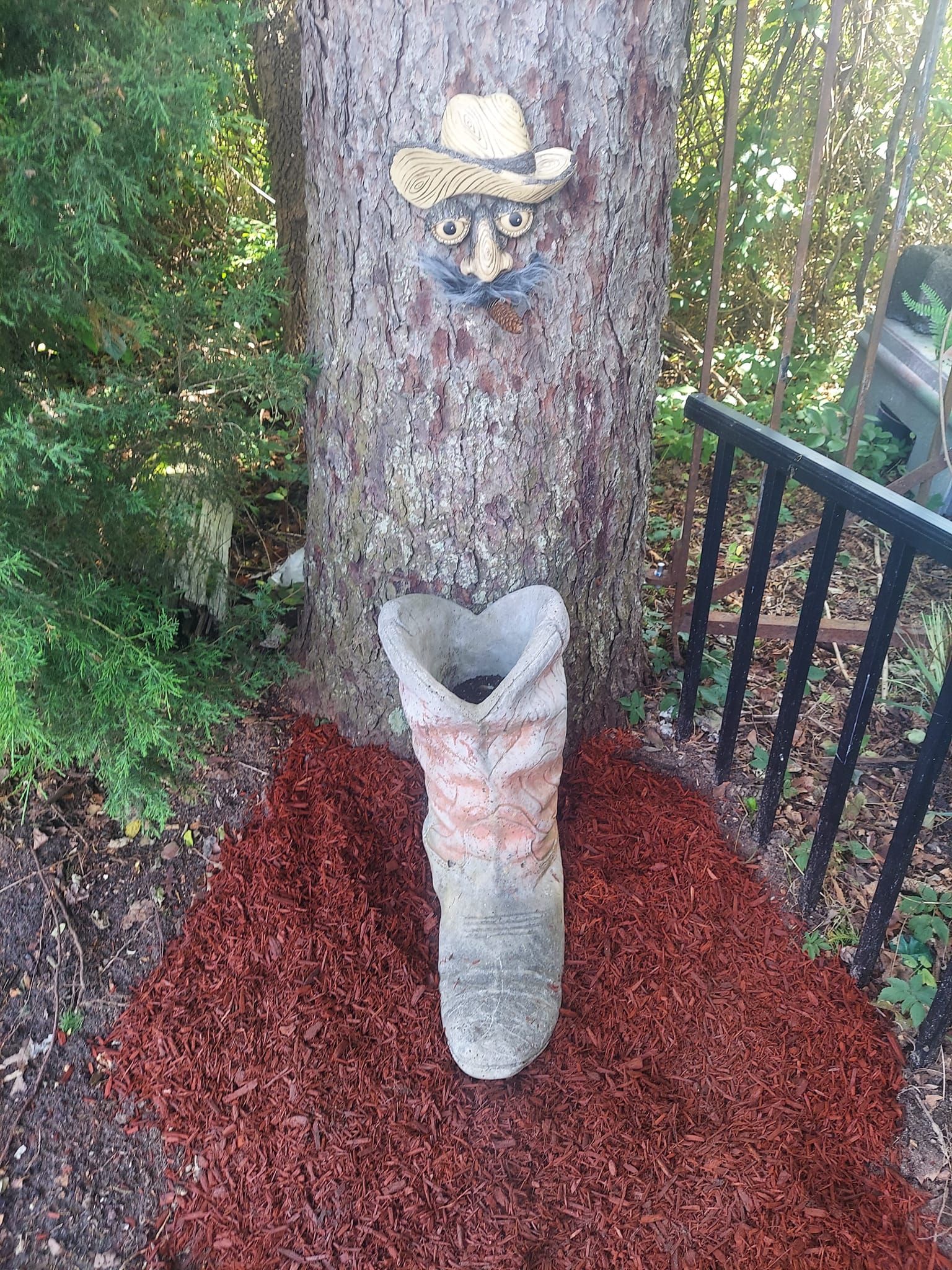 A cowboy boot with a face carved into it is sitting next to a tree.