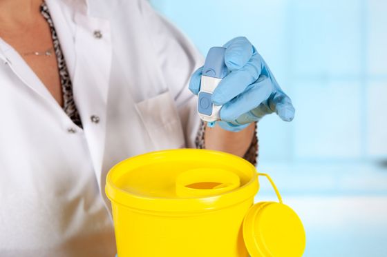 Un medico tiene in mano una siringa e un contenitore giallo.