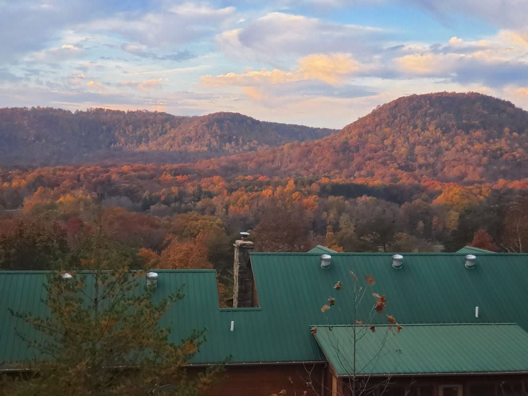Mountain valley at sunset with autumn trees and a green-roofed building in the foreground