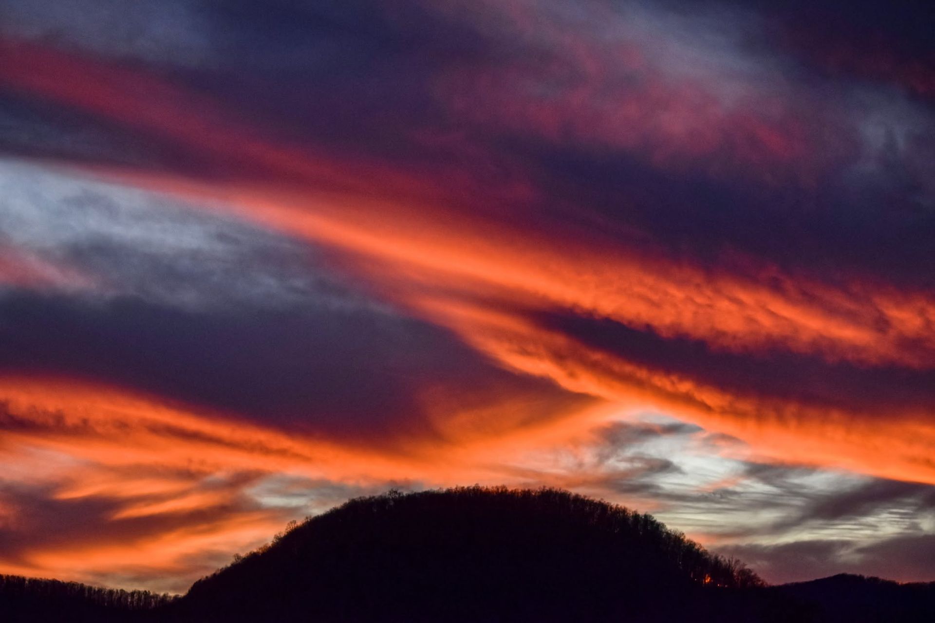 Silhouetted hill under a vivid purple, orange, and red sunset sky with streaked clouds
