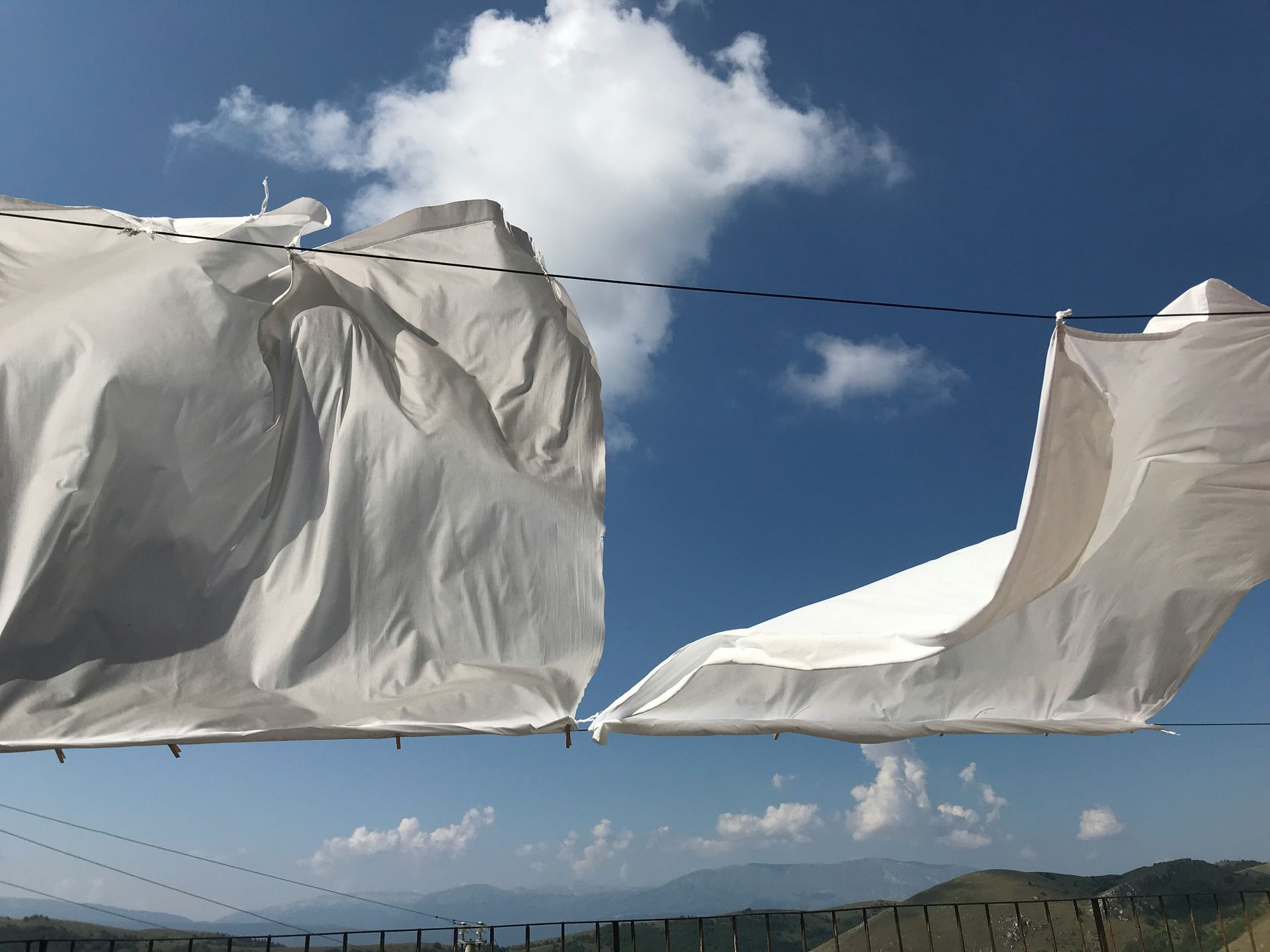 White sheets hanging on a clothesline against a blue sky with clouds and distant mountains