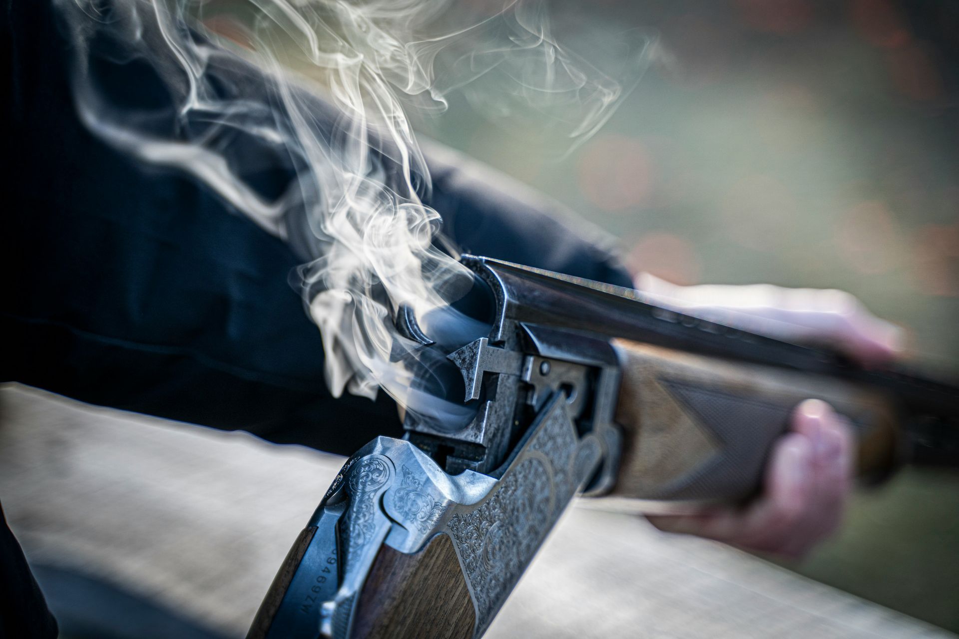 Smoke rises from a black gun being held and aimed outdoors.