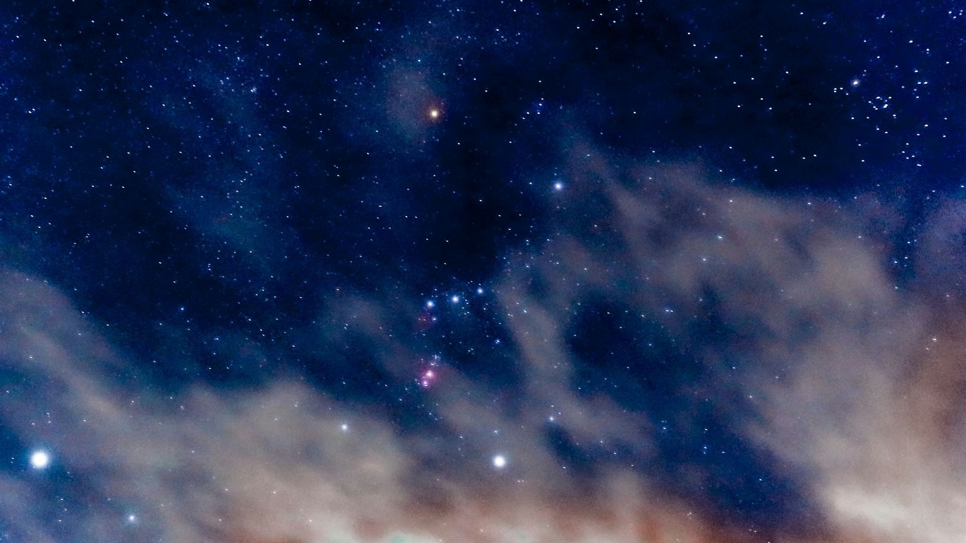 Starry night sky with wispy clouds and faint colorful nebula-like lights