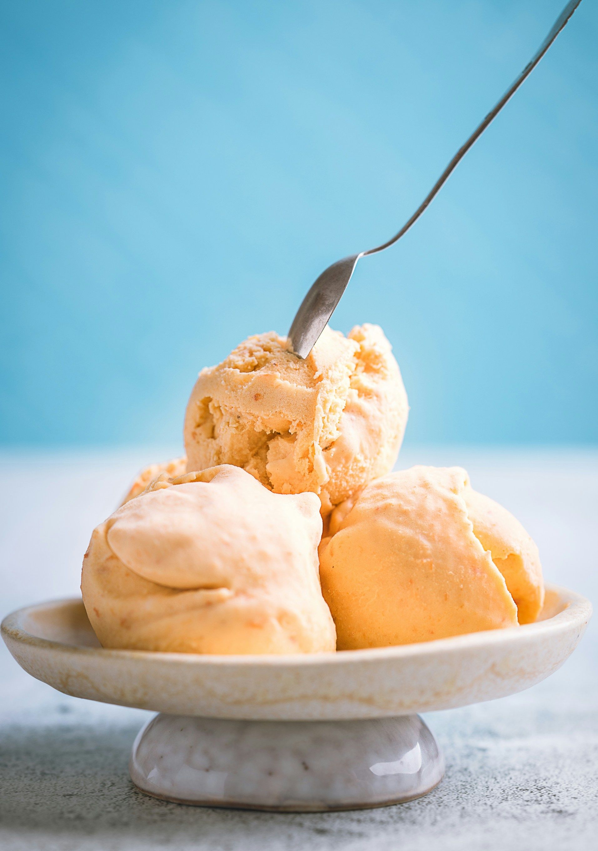 Scoop of vanilla ice cream in a white bowl with a spoon against a blue background