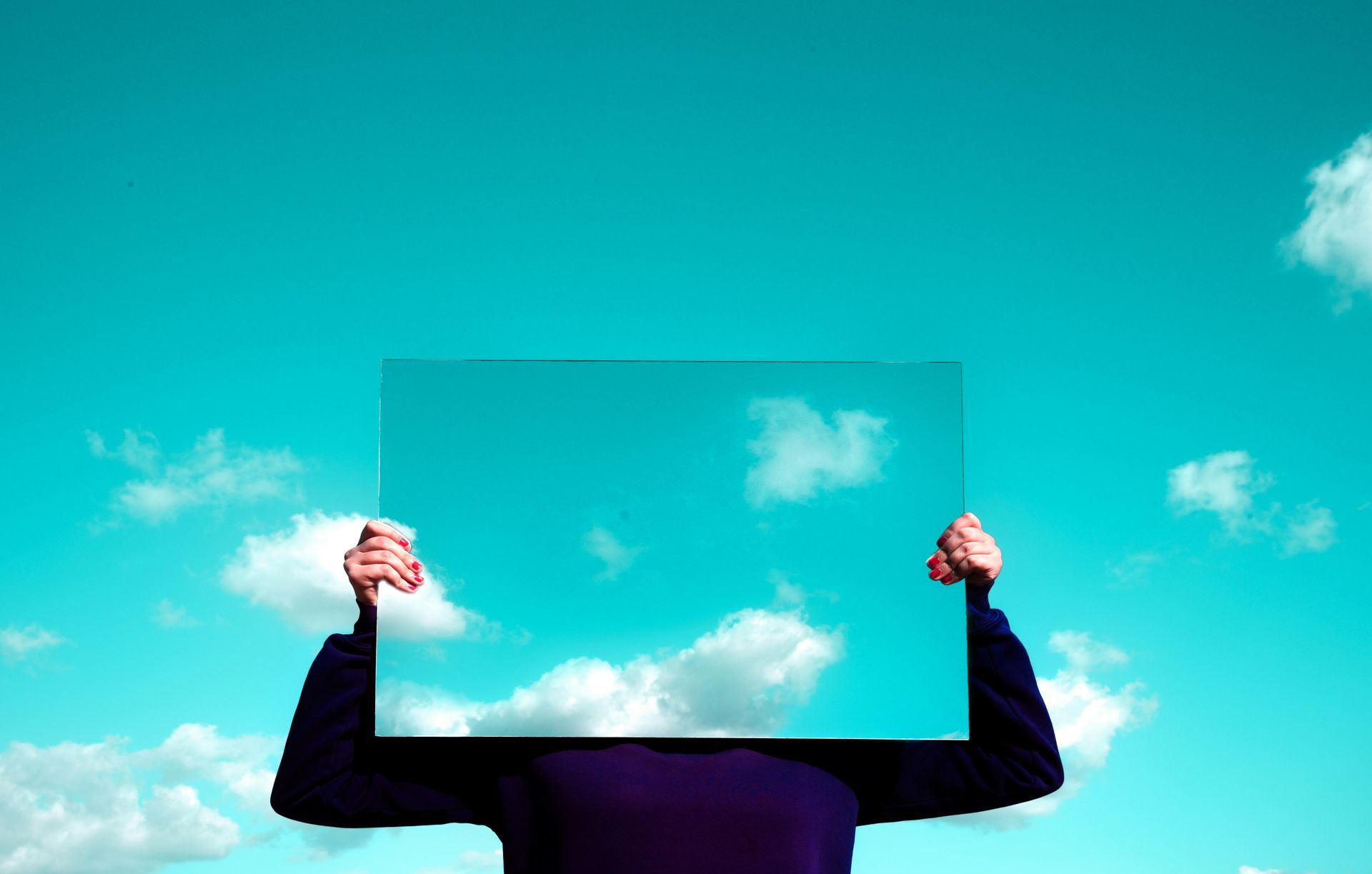 Person holding a clear rectangular panel against a blue sky with clouds