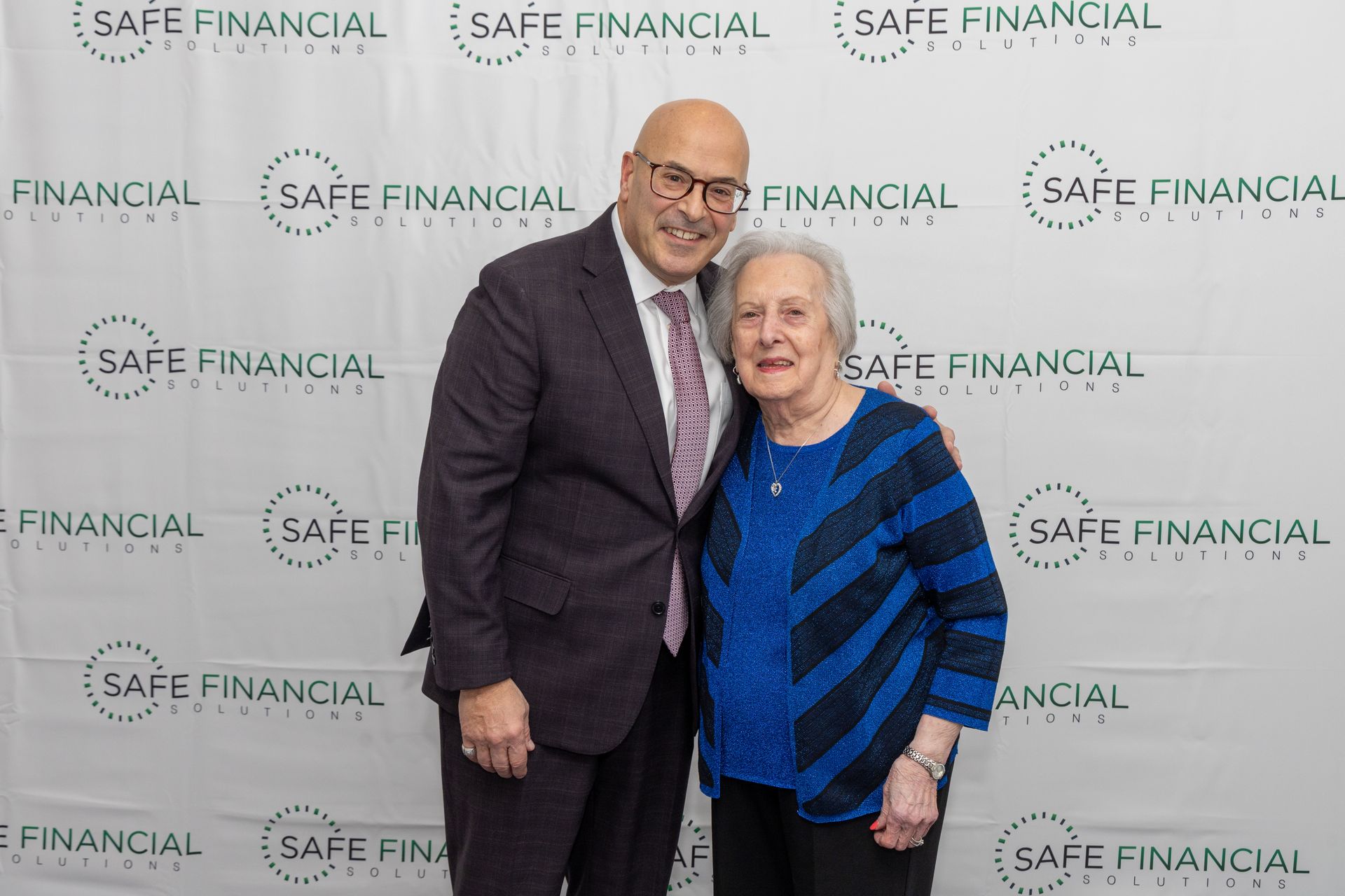 A man and woman smiling in front of a backdrop with a 