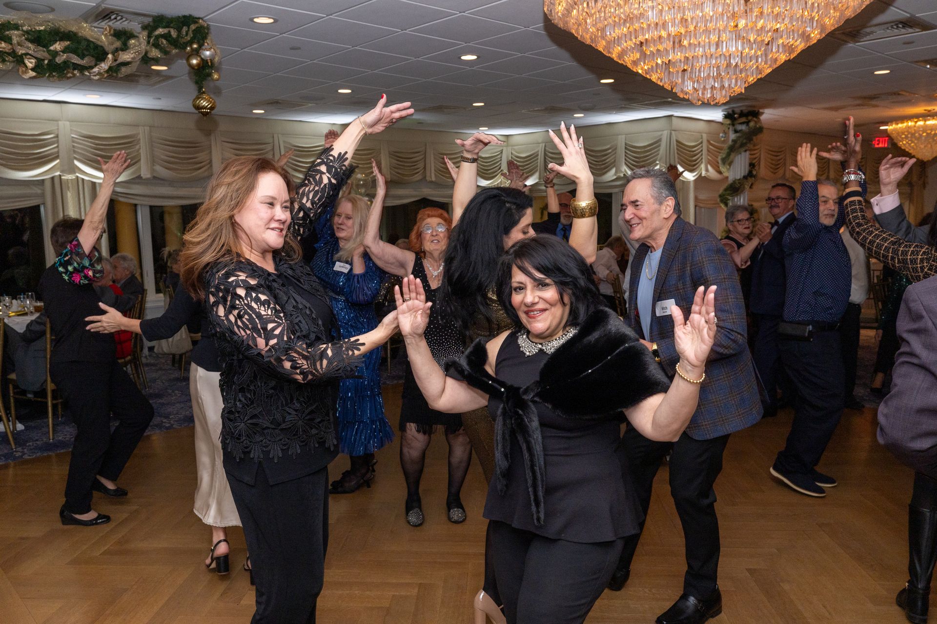 People dancing at a celebratory event in an ornate ballroom with a chandelier.