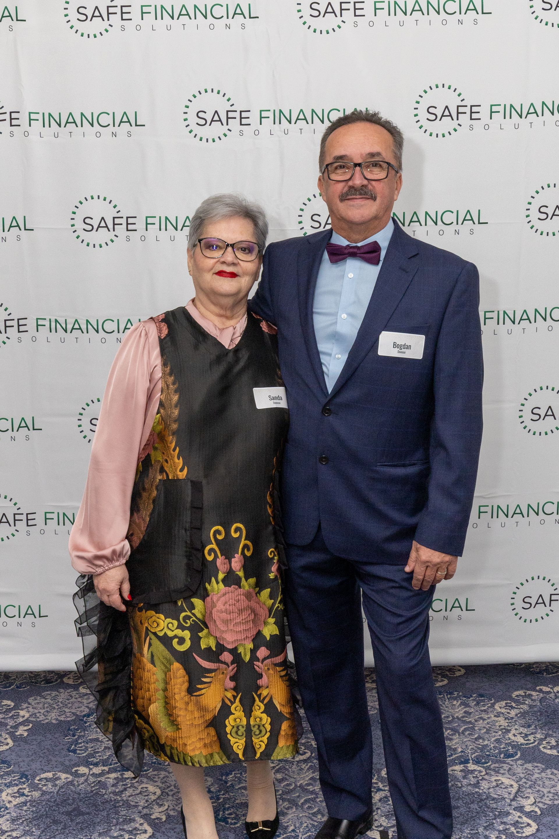 A woman and a man pose in front of a backdrop with 