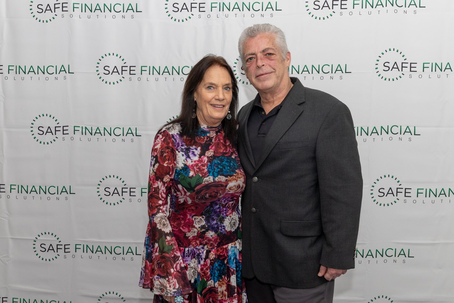 Two people pose in front of a backdrop with 