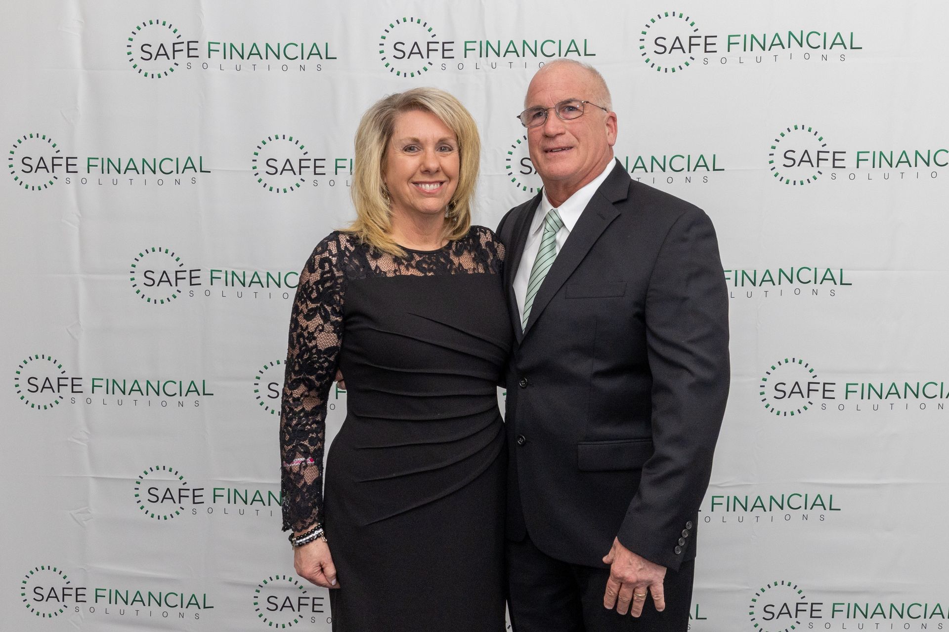 A man and woman pose in front of a backdrop that says 