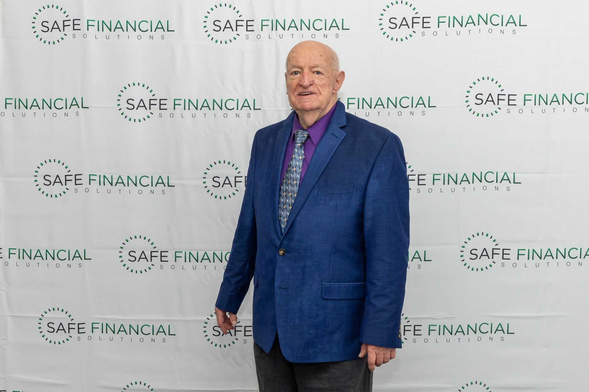 Man in blue blazer stands in front of a backdrop with 