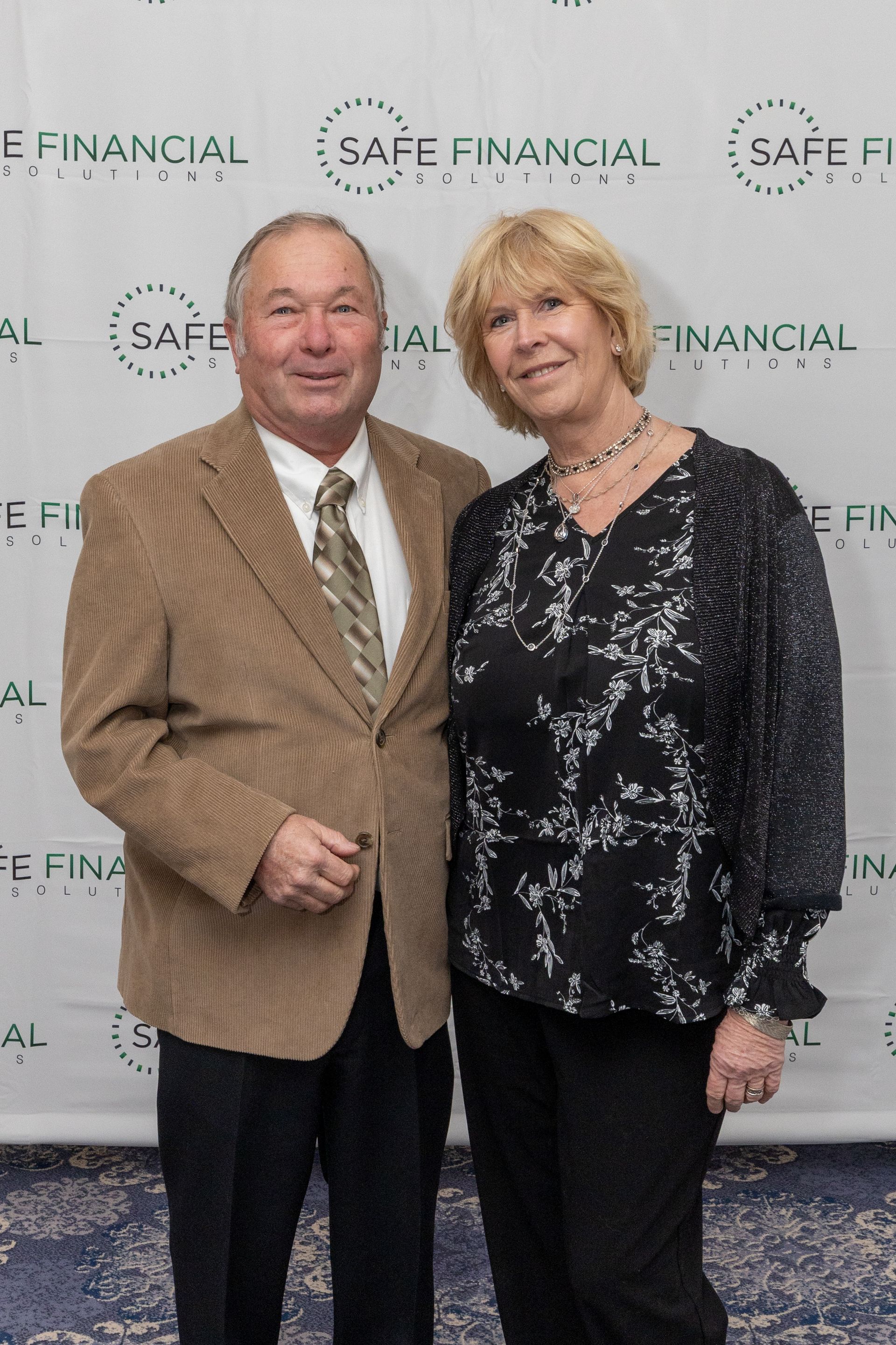A man and woman posing for a photo. The man wears a blazer and tie; 