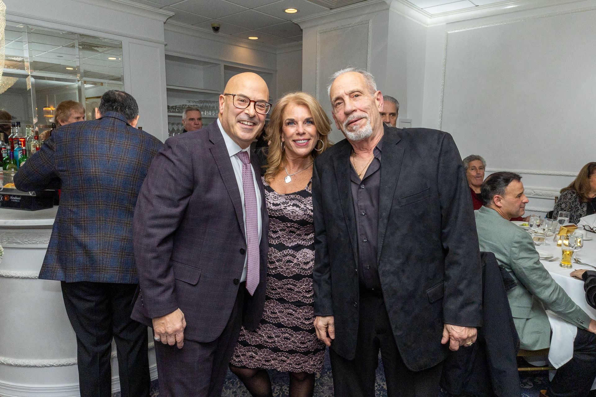 Three people smiling for a photo indoors, one woman in the middle, two men on either side.