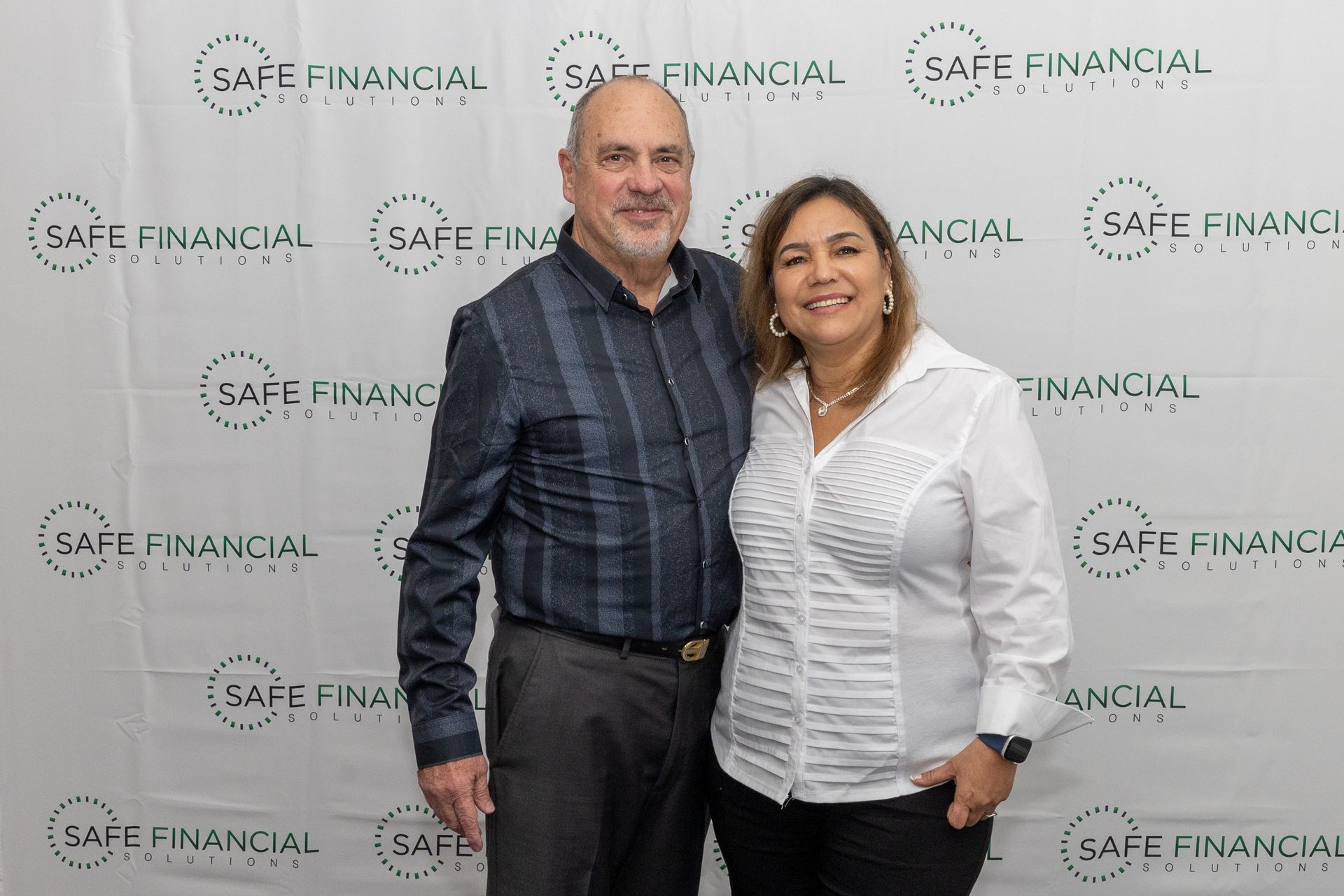 Two people posing in front of a backdrop with the 