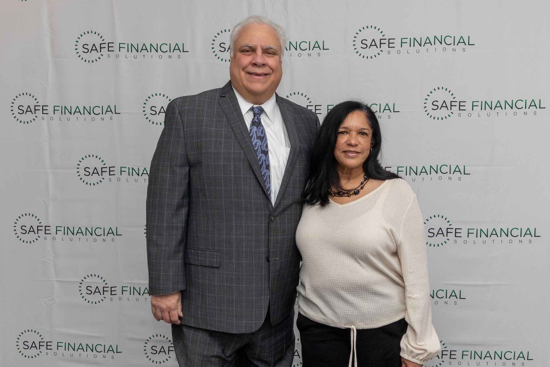 A man and woman posing for a photo in front of a backdrop with a company logo.