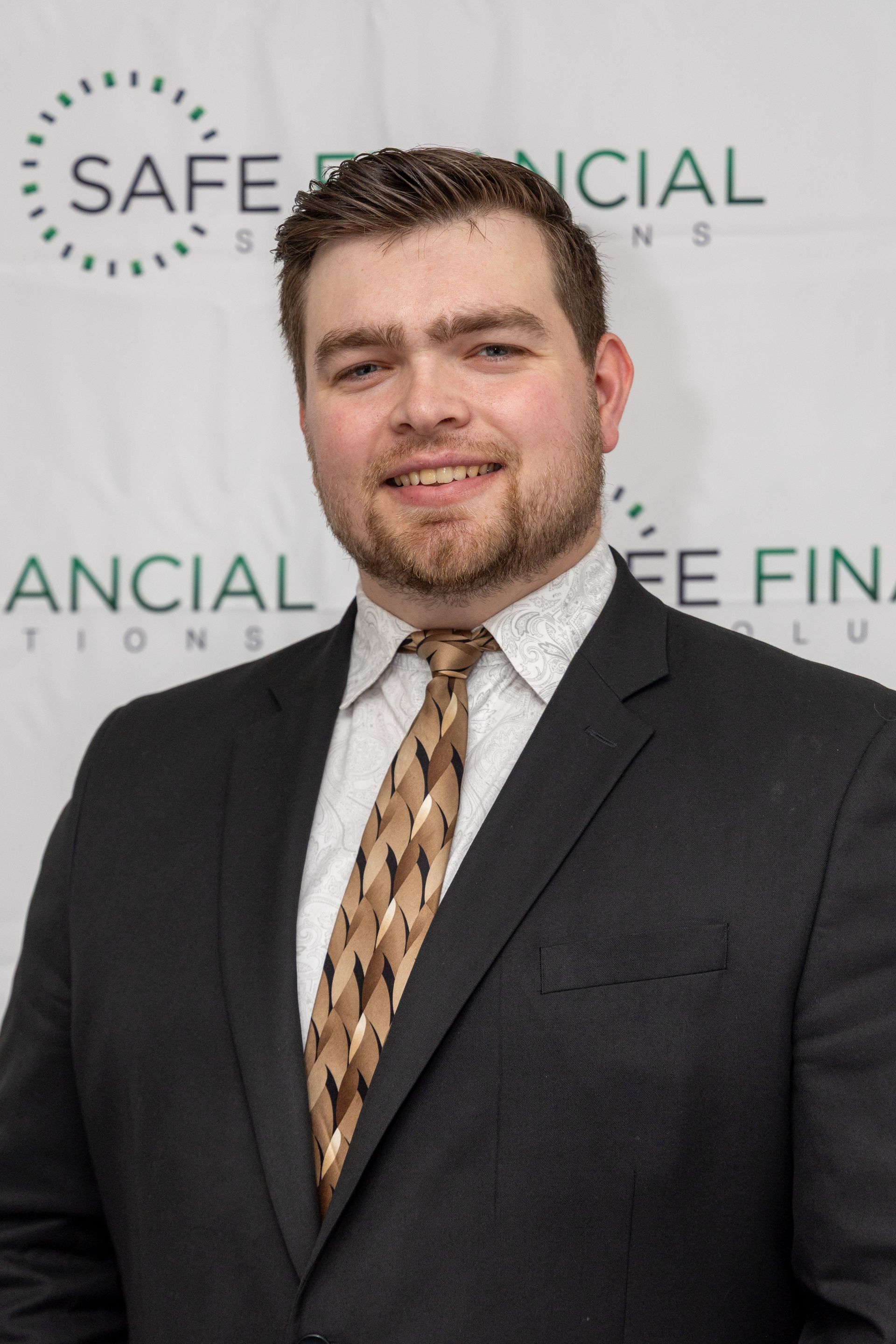 Man in a suit smiles, standing in front of a backdrop with the words 
