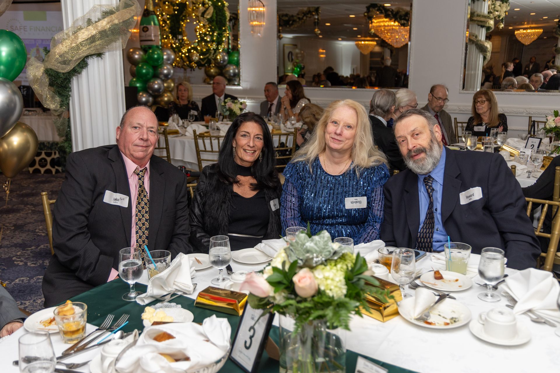 Four people sit at a table in a decorated banquet hall. They smile and look at the camera.
