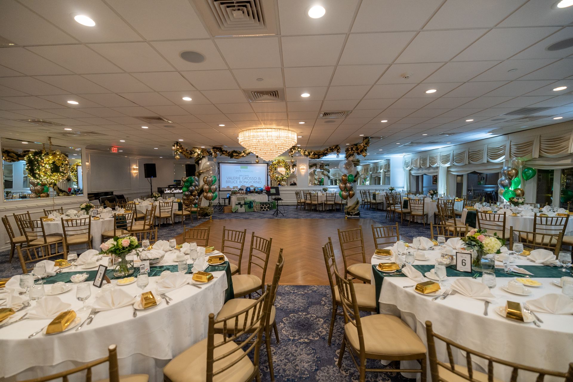 Ballroom set for an event with round tables, chairs, and a chandelier; decorations in green and gold.